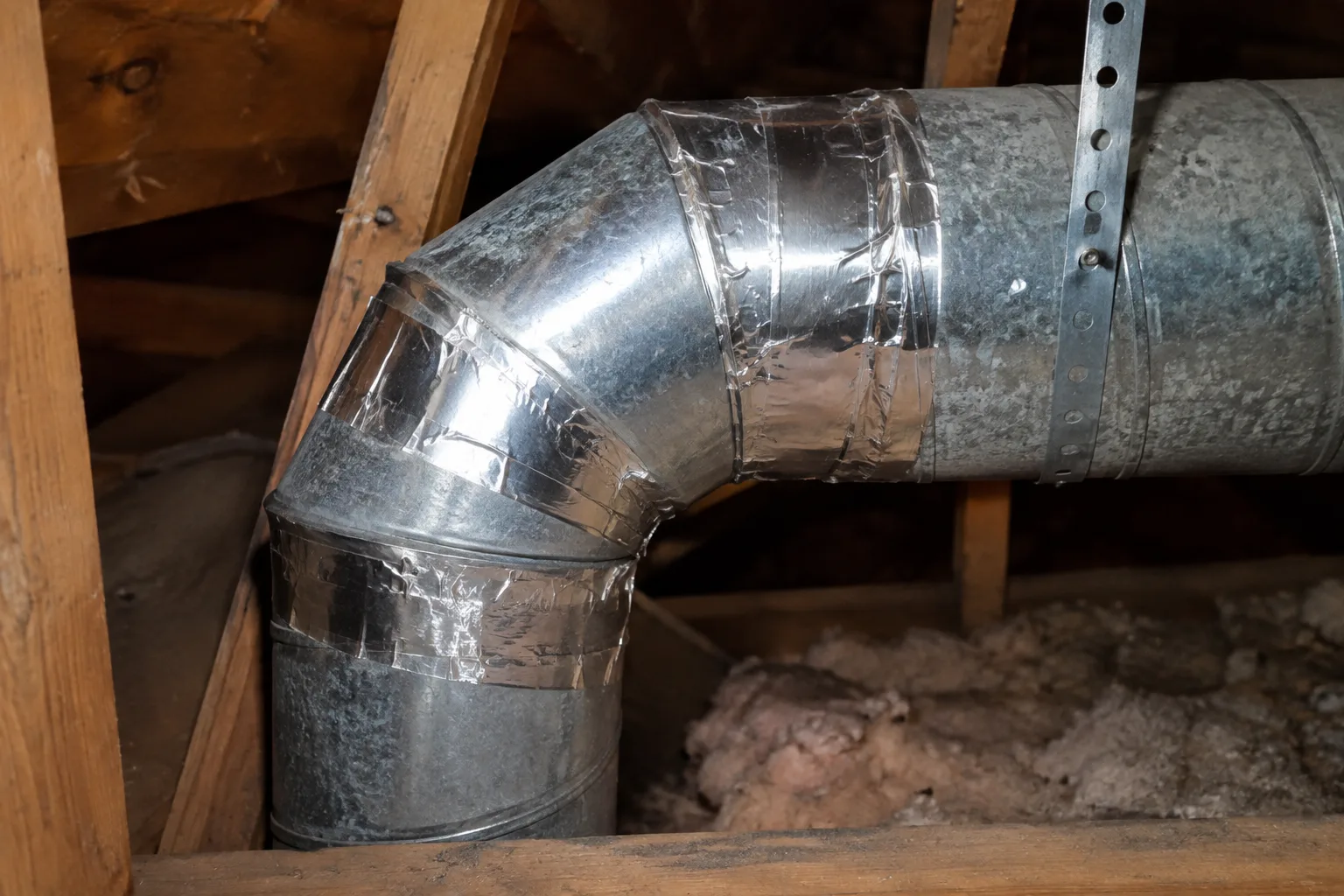 Close-up of a sheet-metal duct elbow joint in an attic, freshly taped and sealed at each connection after a repair.