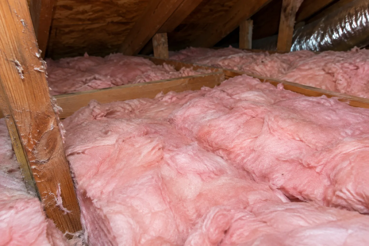 Close-up of pink fiberglass batt insulation evenly filling attic floor joist bays for consistent thermal coverage.