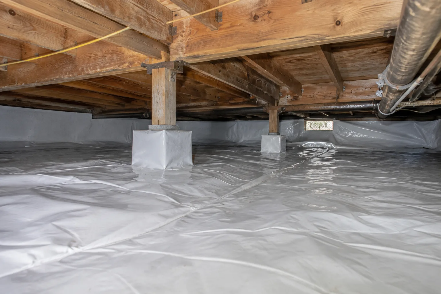 A crawl space fully lined with a vapor moisture barrier, with support piers wrapped in sealed sheeting to block ground moisture.